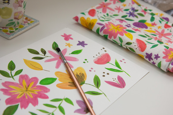 Painted gouache flowers and a paintbrush next to the tea towel