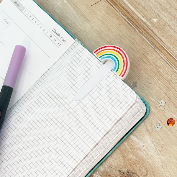 Colourful rainbow planner clip marking a page in a notebook