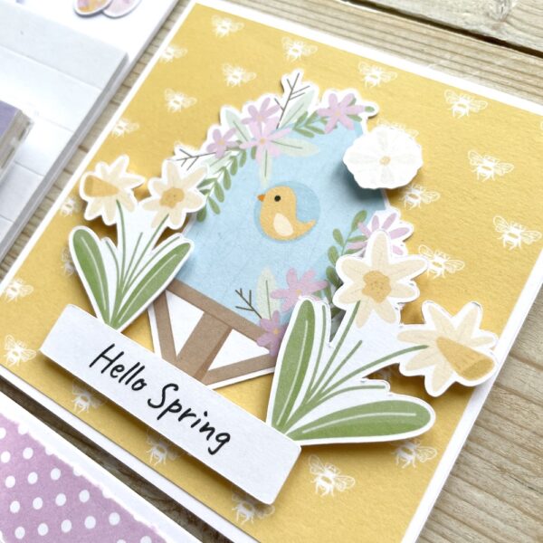 Hello Spring handmade card with yellow patterned bee paper background and cute bird in a birdhouse surrounded by daffodils